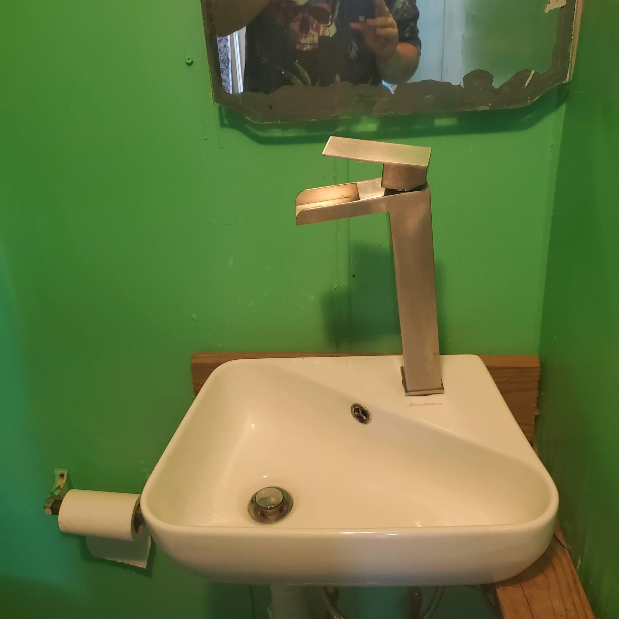 Ein weißes Waschbecken mit einem Wasserhahn, ein Spiegel darüber und eine Holzablage.