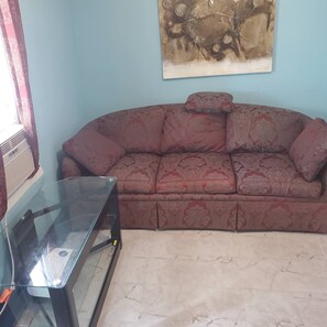 A living room with a sofa, a glass coffee table, and a wall-mounted artwork. - Rustic1BRPet&420 Friendly2.5blocksToBoardsSeptSpecialsProm&SeniorWks22Under25ok (Wildwood)