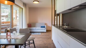 Una cucina moderna con piano cottura integrato, zona pranzo con tavolo e sedie, e un divano sullo sfondo.