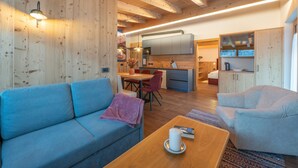 A modern interior with a sofa, dining table, and kitchen area. - 3-Room Apartment Erta with Mountain View, Wi-Fi & Terrace (San Vigilio di Marebbe)