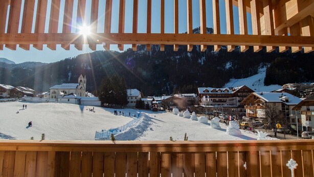 A wooden balcony overlooking a snowy ski slope with buildings in the background. - 3-Room Apartment Erta with Mountain View, Wi-Fi & Terrace (San Vigilio di Marebbe)