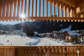 A wooden balcony overlooking a snowy ski slope with buildings in the background. - 3-Room Apartment Erta with Mountain View, Wi-Fi & Terrace (San Vigilio di Marebbe)