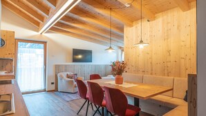 A modern kitchen with wooden cabinets, a dining area with a wooden table and red chairs, and a built-in bench. - 3-Room Apartment Erta with Mountain View, Wi-Fi & Terrace (San Vigilio di Marebbe)