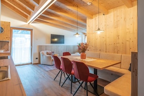 A modern kitchen with wooden cabinets, a dining area with a wooden table and red chairs, and a built-in bench.