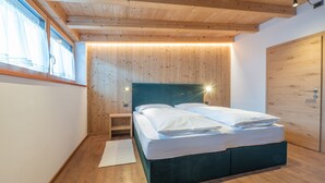 A bedroom with a wooden ceiling, a bed with white linens, a nightstand, and a wooden wardrobe. - 3-Room Apartment Erta with Mountain View, Wi-Fi & Terrace (San Vigilio di Marebbe)
