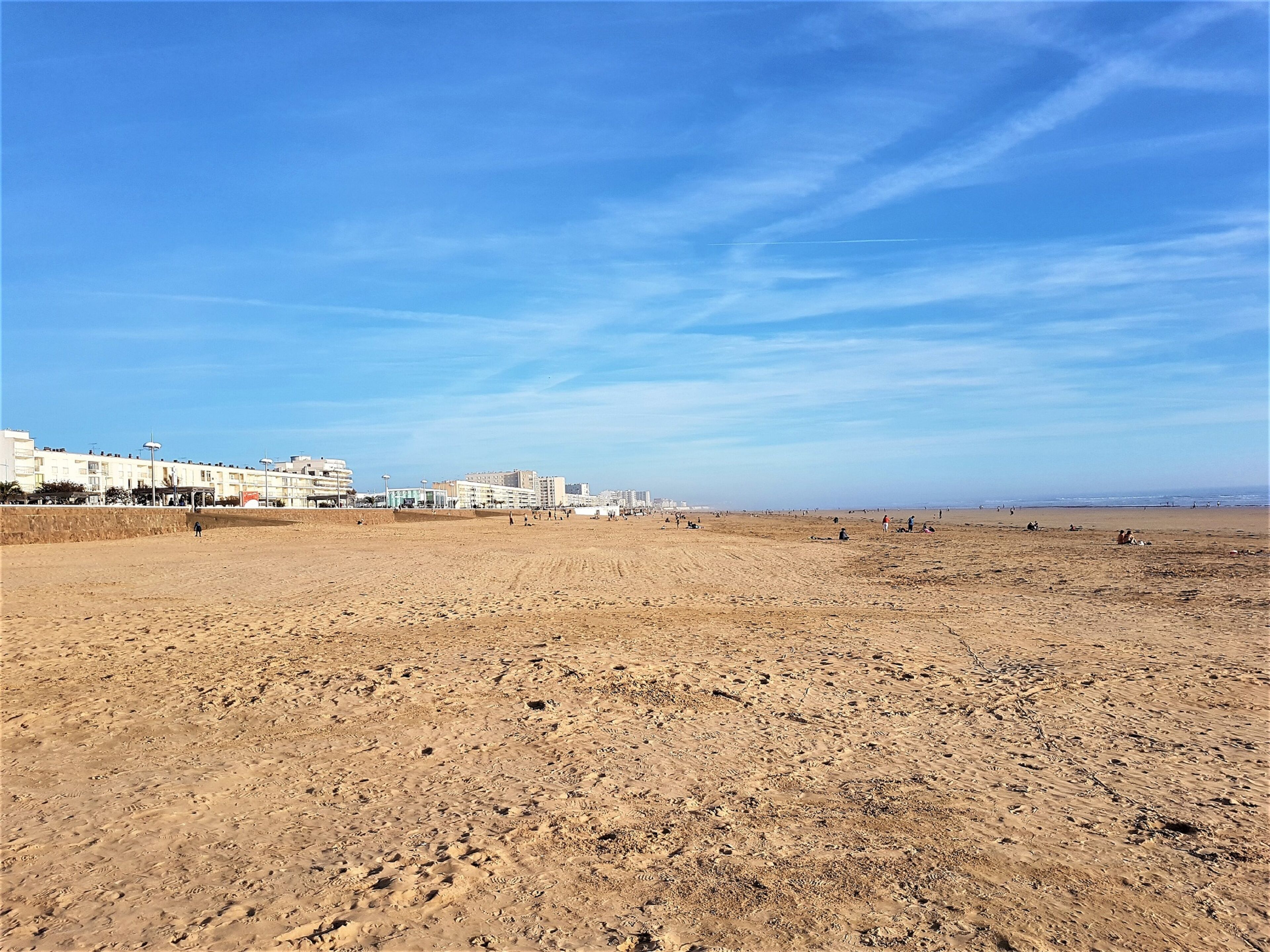 Ein weiter Sandstrand mit Gebäuden im Hintergrund.
