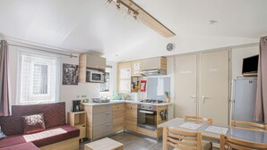 Eine kleine Küchenzeile mit Mikrowelle, Herd und Backofen. Es gibt einen Essbereich mit Tisch und Stühlen sowie ein Sofa mit Kissen.