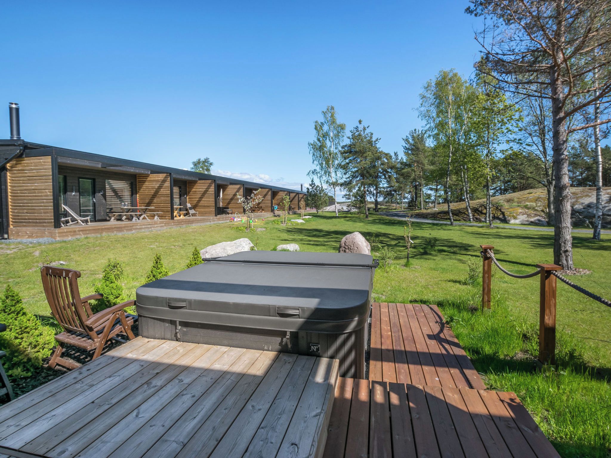 A wooden deck with a hot tub, outdoor seating, and a building with large windows.