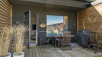 En träaltan med ett bord och stolar, en grill och krukväxter.