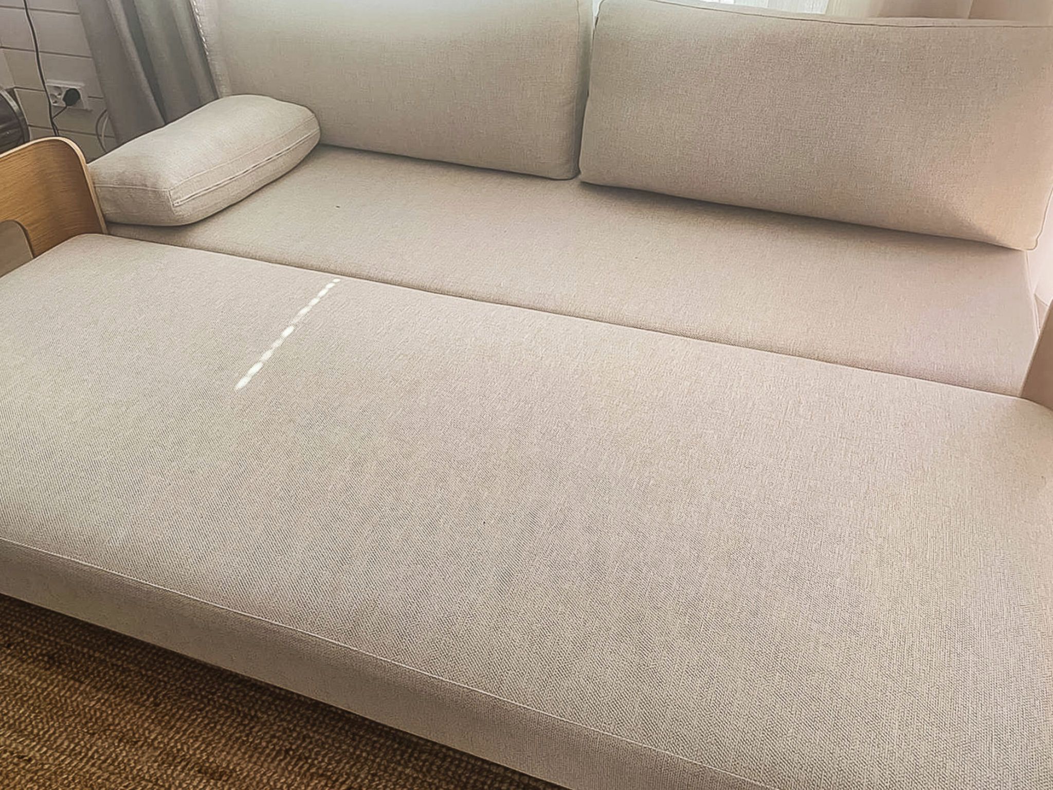 Un canapé beige recouvert d’un tissu texturé, une chaise en bois et un tapis marron.