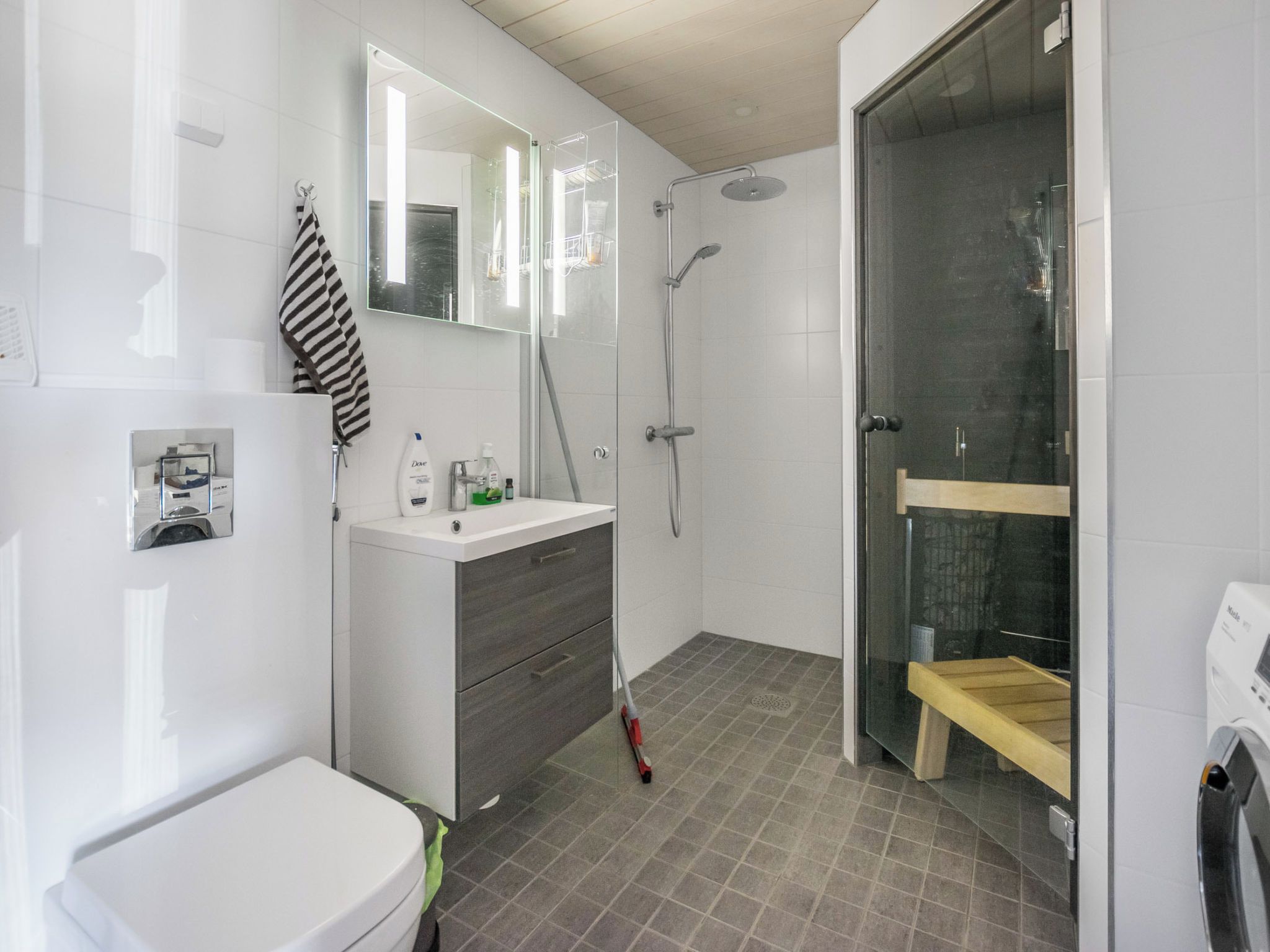 Un baño moderno con inodoro, tocador con espejo, zona de ducha con puerta de cristal y banco de madera.