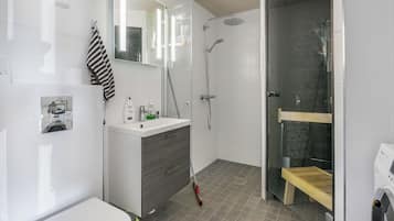 A modern bathroom with a toilet, a vanity with a mirror, a shower area with a glass door, and a wooden bench.