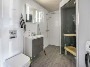Un baño moderno con inodoro, tocador con espejo, zona de ducha con puerta de cristal y banco de madera.