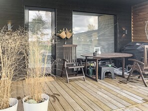 A wooden deck with a table and chairs, potted plants, and a grill.