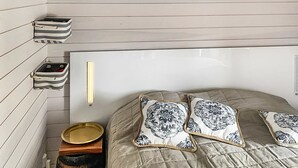 A cozy room with a bed, two pillows with a patterned design, a bedside table with a bowl, and a small storage box on the wall.