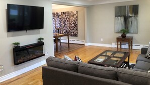A living room with a flat-screen TV, a fireplace, a sofa, a coffee table, and a dining area with a table and chairs. - Niagara Executive Luxury - HUGE, Warm, Cozy and Clean 3 Bed, 1 Bath SuiteStay(1) (Welland)