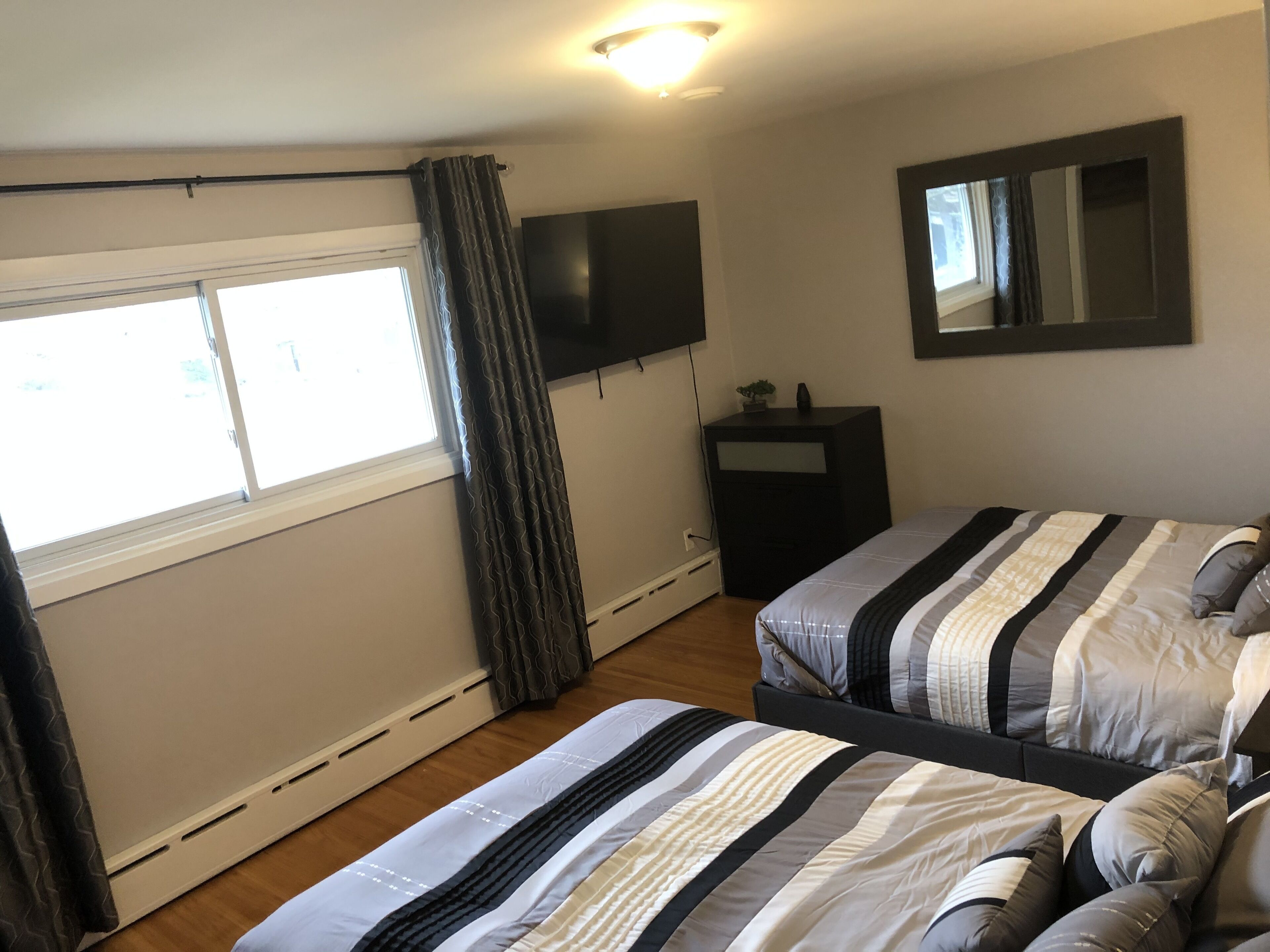Quarto com duas camas, televisão, penteadeira, janela com cortinas e espelho na parede.