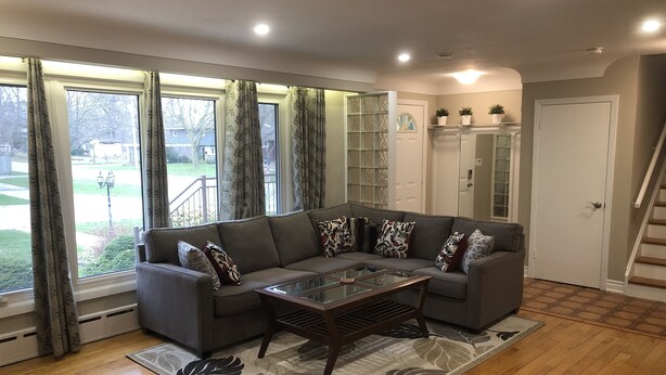 A living room with a sectional sofa, a glass coffee table, and a patterned rug. - Niagara Executive Luxury - HUGE, Warm, Cozy and Clean 3 Bed, 1 Bath SuiteStay(1) (Welland)