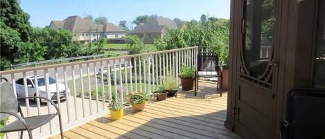 A wooden deck with potted plants, a chair, and a view of houses in the background.