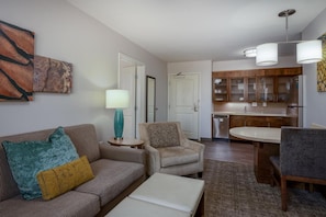 A living room with a sofa, armchair, coffee table, and a dining area with a table and chairs. There is a kitchen in the background with cabinets and a refrigerator. - Staybridge Suites Phoenix East - Gilbert, an IHG Hotel (Gilbert)