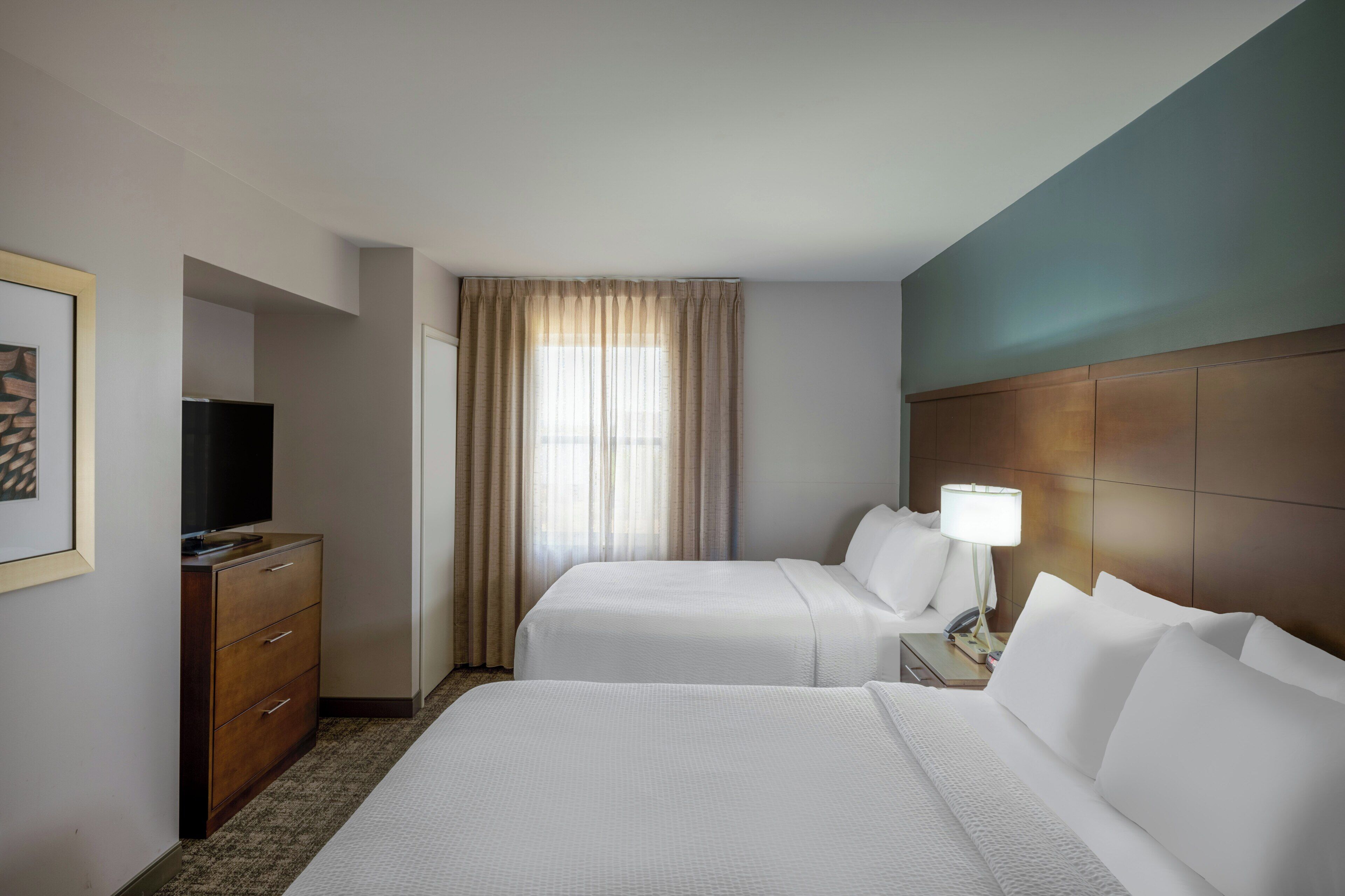 A hotel room with two beds, a TV, a dresser, and a window with curtains.