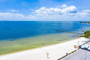 A beach with clear waters, a pier, and a white sandy shore.