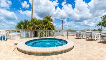 A circular pool with a brick border, surrounded by a white fence, palm trees, and a clear blue sky.