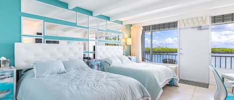 Habitación de hotel con dos camas, un balcón con vistas y una pequeña zona de estar.