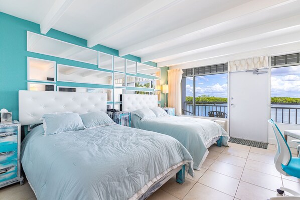 A hotel room with two beds, a balcony with a view, and a small seating area.