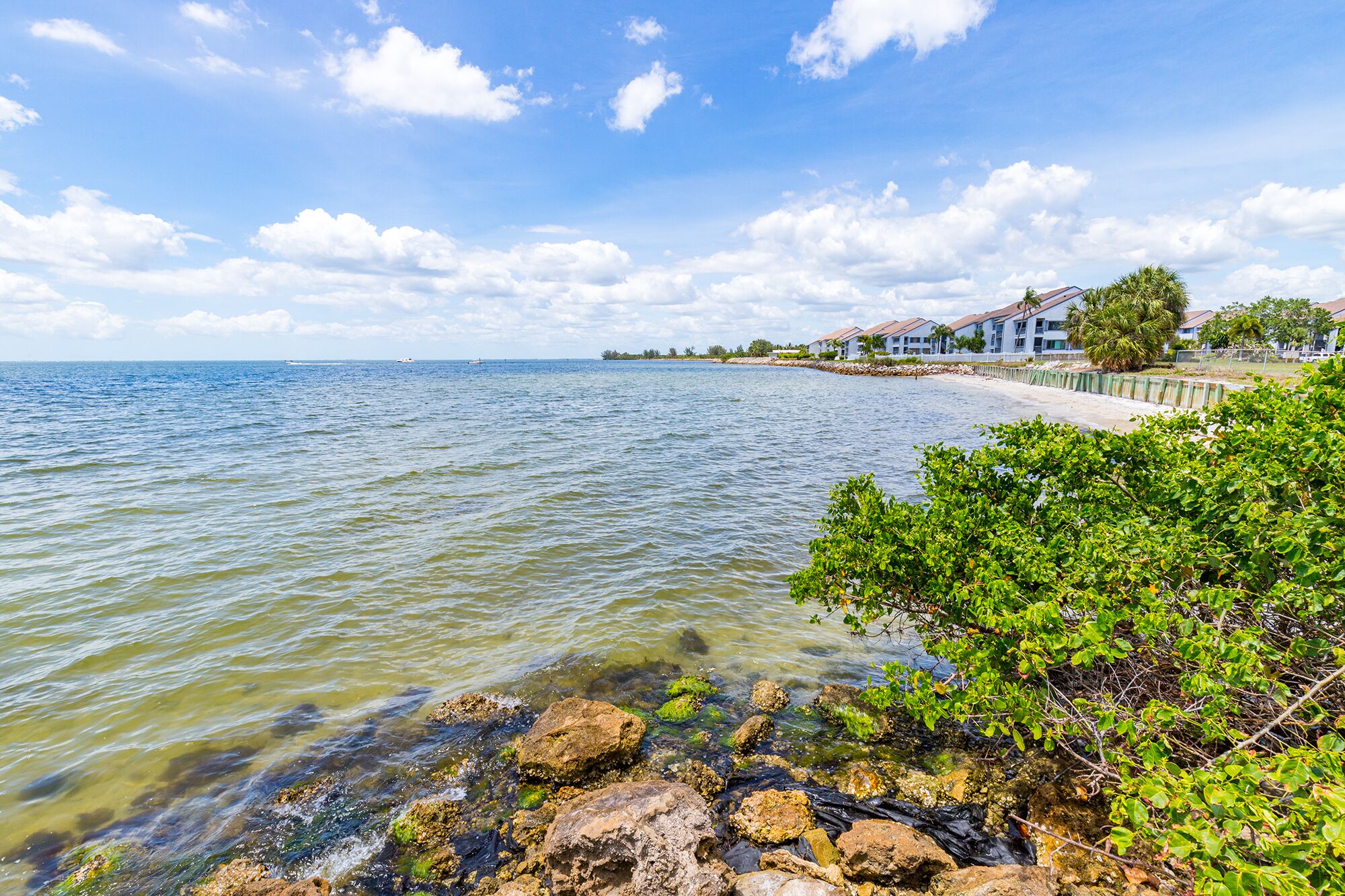 A coastal view with clear water, a sandy beach, and a row of buildings along the shore.