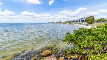 A coastal view with clear water, a sandy beach, and a row of buildings along the shore.