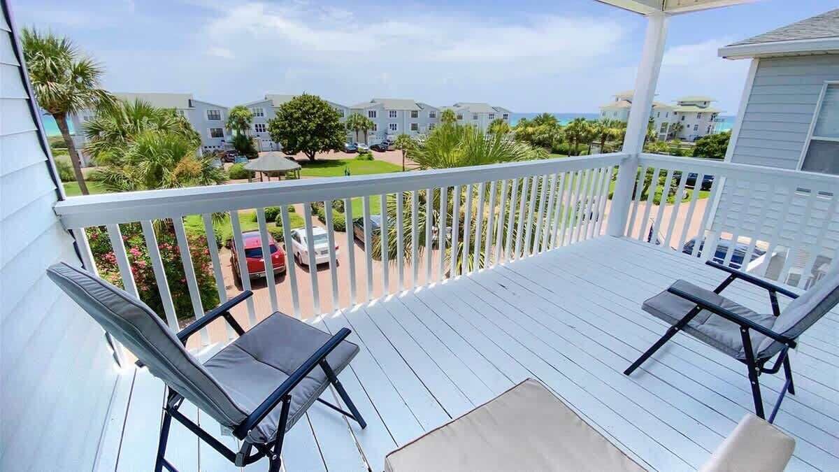 A balcony with two chairs and a table, overlooking a residential area with houses and a clear sky.