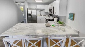 A modern kitchen with white cabinetry, a marble island, and a 'Welcome to our Beach House' sign.