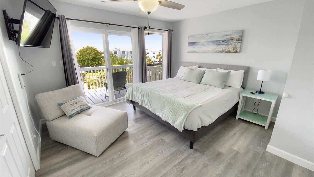 A bedroom with a bed, a chair, a TV, a balcony, and a painting on the wall.