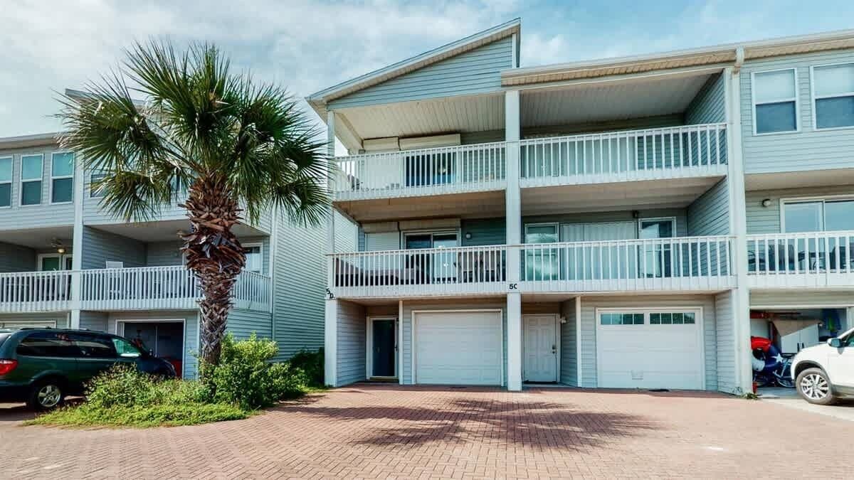 Un edificio residencial de varios pisos con balcones, una palmera y coches aparcados.