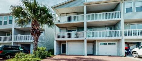 Un edificio residencial de varios pisos con balcones, una palmera y coches aparcados.