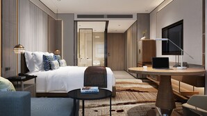 Une chambre d’hôtel moderne équipée d’un lit, d’un bureau, d’une chaise, d’une télévision et d’une petite table sur laquelle se trouve un livre.