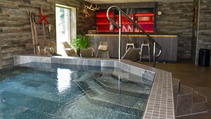 An indoor swimming pool with clear water, surrounded by stone walls and a bar area with red shelves. - BigRiverCamp Hotel & Spa (Föllinge)