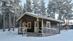 A wooden cabin with a porch and steps, surrounded by snow-covered trees. - BigRiverCamp Hotel & Spa (Föllinge)