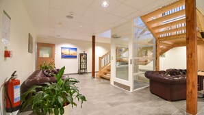 A lobby with a fire extinguisher, a brown leather sofa, a potted plant, and a staircase. - BigRiverCamp Hotel & Spa (Föllinge)