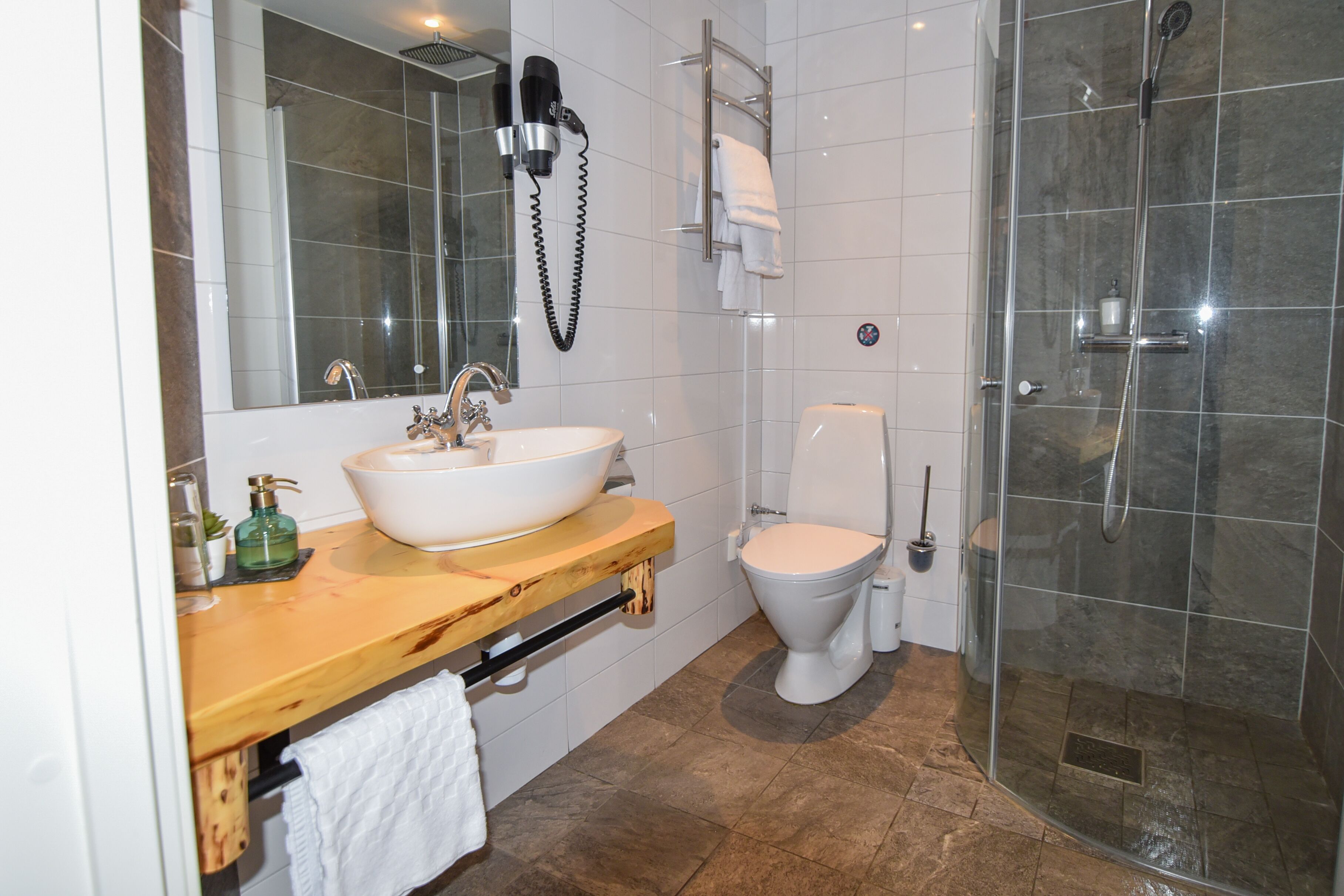 Un baño con tocador de madera, un lavabo blanco, inodoro y ducha con mampara de vidrio.