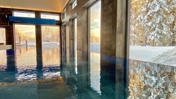 An indoor swimming pool with clear water, large windows, and a view of a snowy landscape. - BigRiverCamp Hotel & Spa (Föllinge)