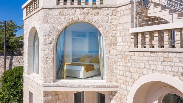 Ein Steinhaus mit einem Schlafzimmer, das ein großes Rundbogenfenster und einen Balkon hat.