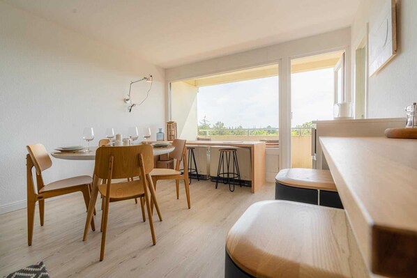 Une cuisine moderne avec des plans de travail en bois, un coin repas avec des chaises en bois et une grande fenêtre donnant sur l’extérieur.