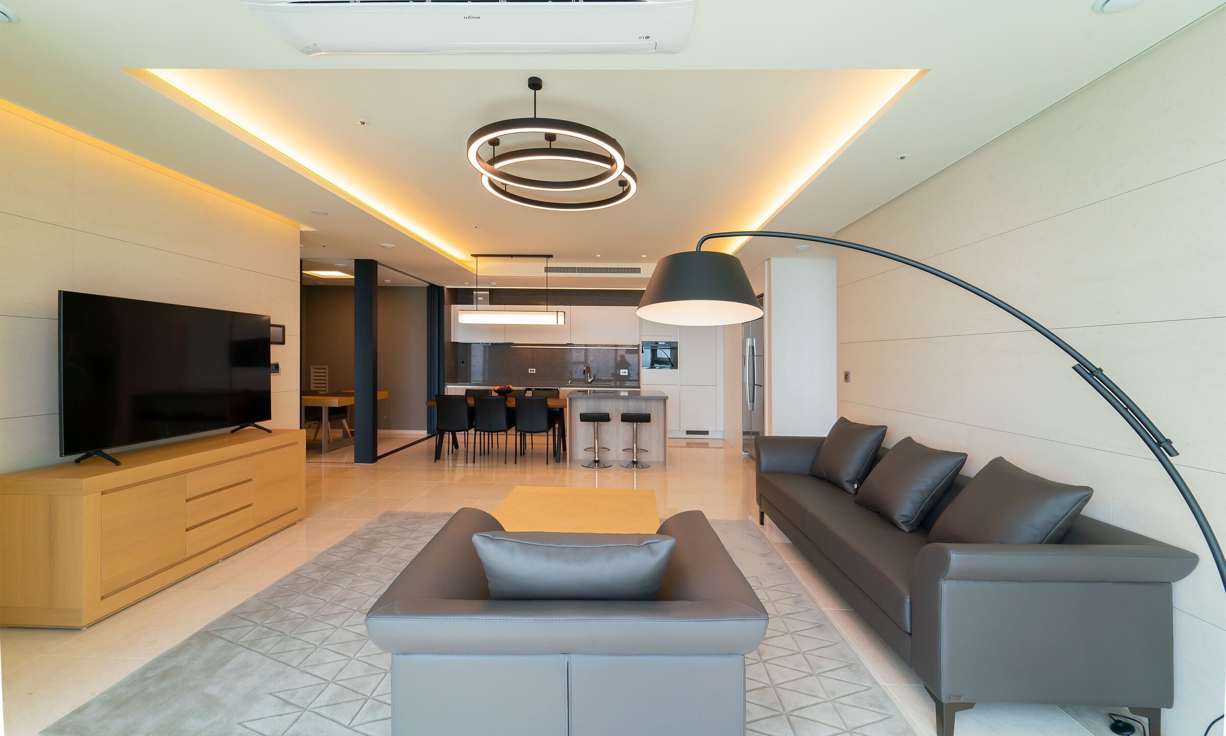 Een moderne woonkamer met een flatscreen televisie, een bank en een eethoek, met een keuken op de achtergrond.