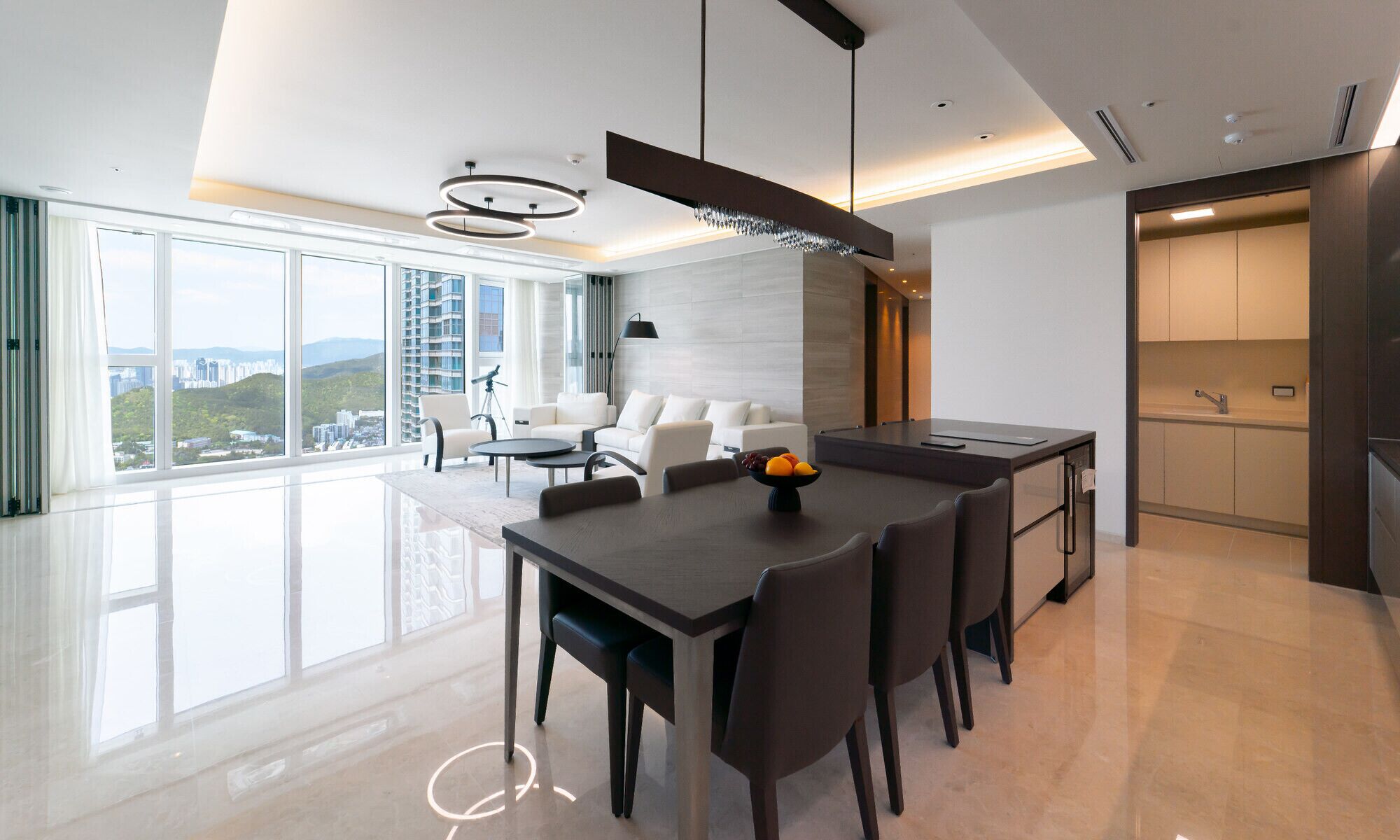 A modern dining area with a large table, chairs, and a fruit bowl.