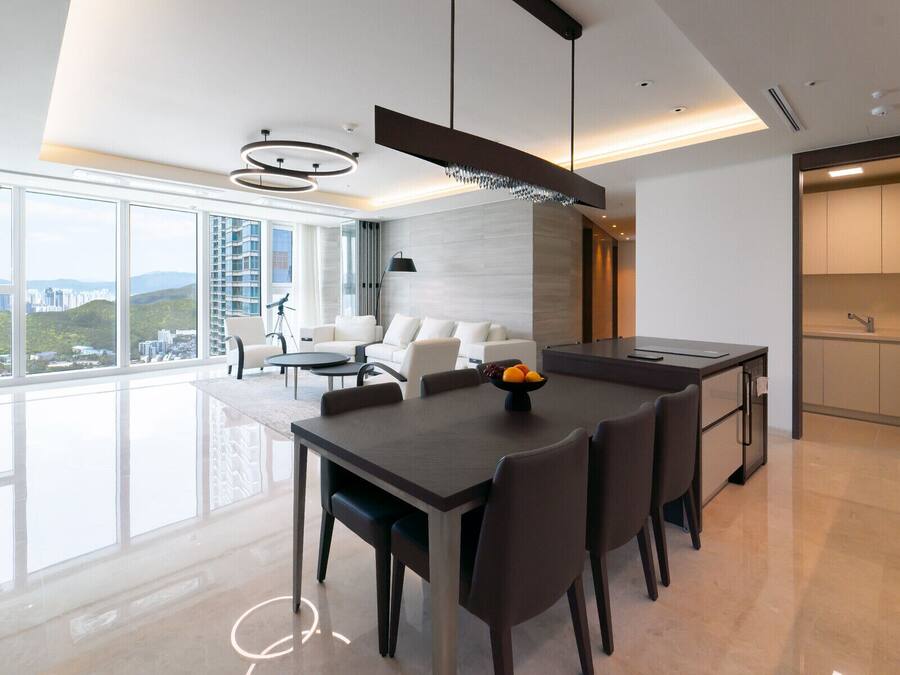 A modern dining area with a large table, chairs, and a fruit bowl.