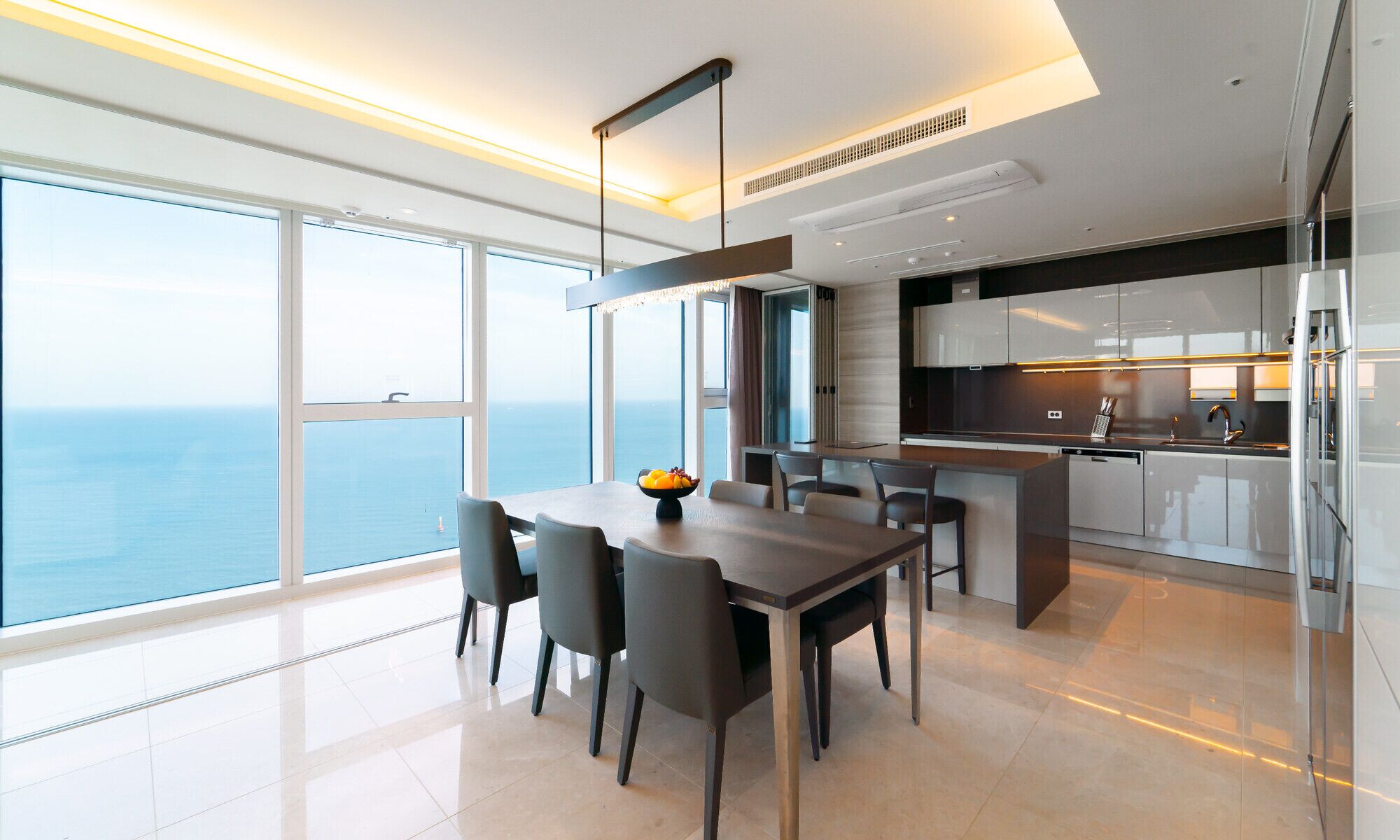 A modern kitchen with a view of the sea, a dining area with a table and chairs, and a large window.