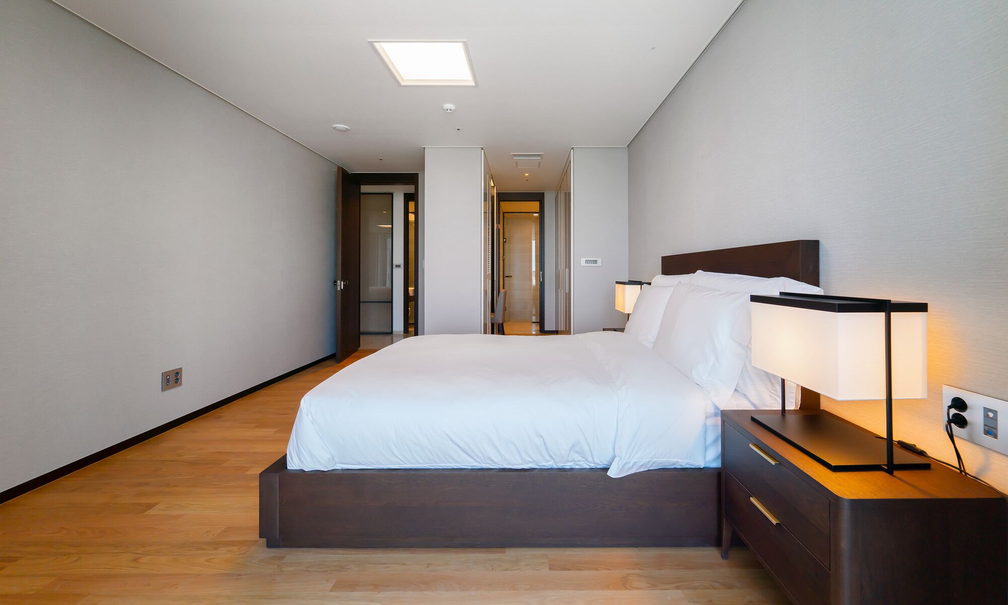 A modern hotel room with a large bed, bedside lamps, and a wooden floor.