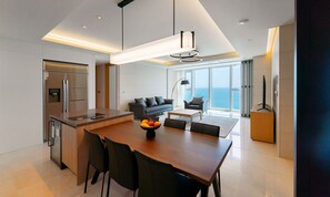 A modern kitchen with a central island, dining area with chairs, a sofa, and a view of the sea. -  NEWCZ LCT RESIDENCE (Busan)